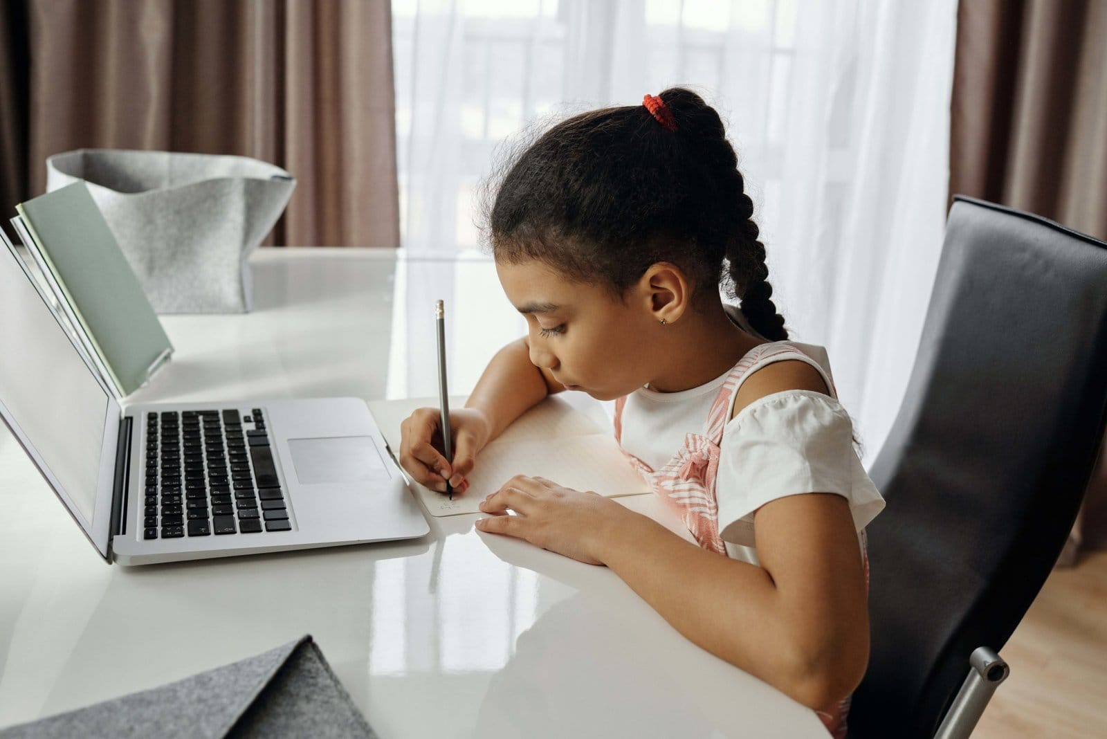 A girl writing in a notebook with a laptop open on the desk