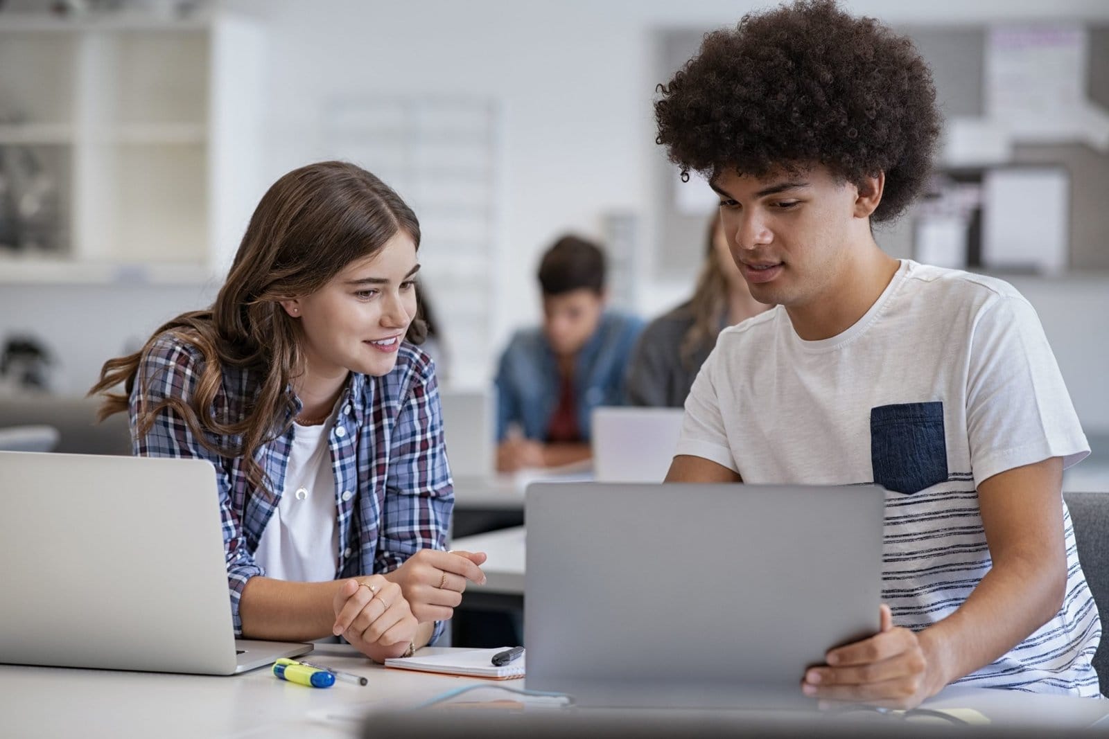 Two students working together on laptops in a classroom