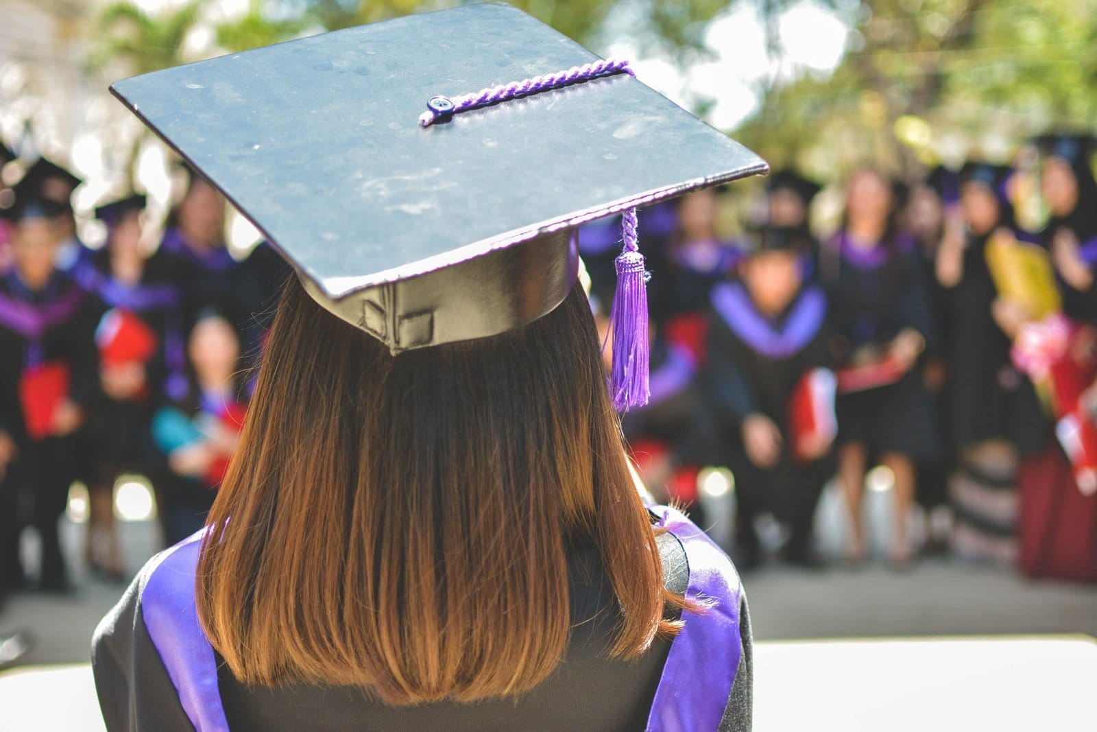 The back of a graduate in a cap and gown facing a crowd of other graduates